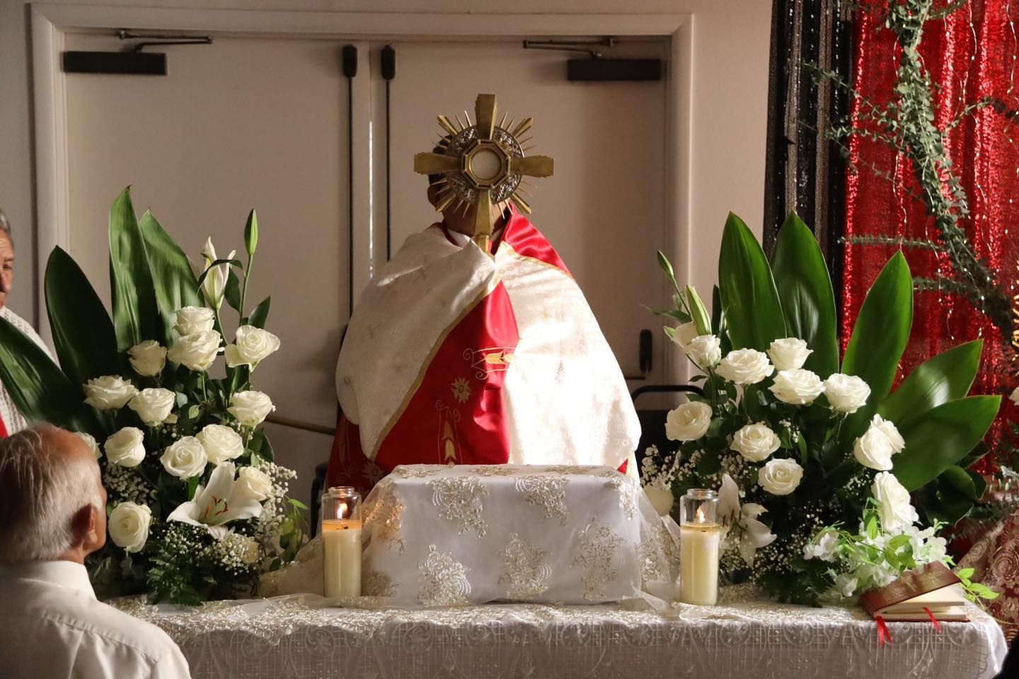 Religious altar with a white-and-red cloth, flowers, candles, and a small statue in a chapel.