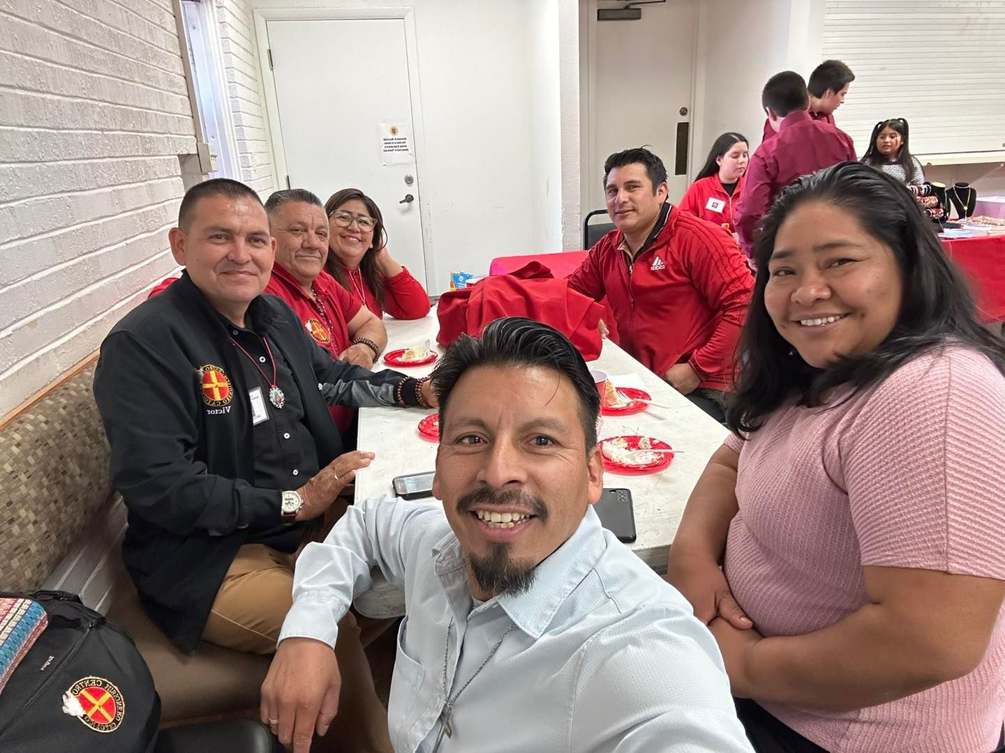 People seated at a table in a casual restaurant, smiling for a group selfie.