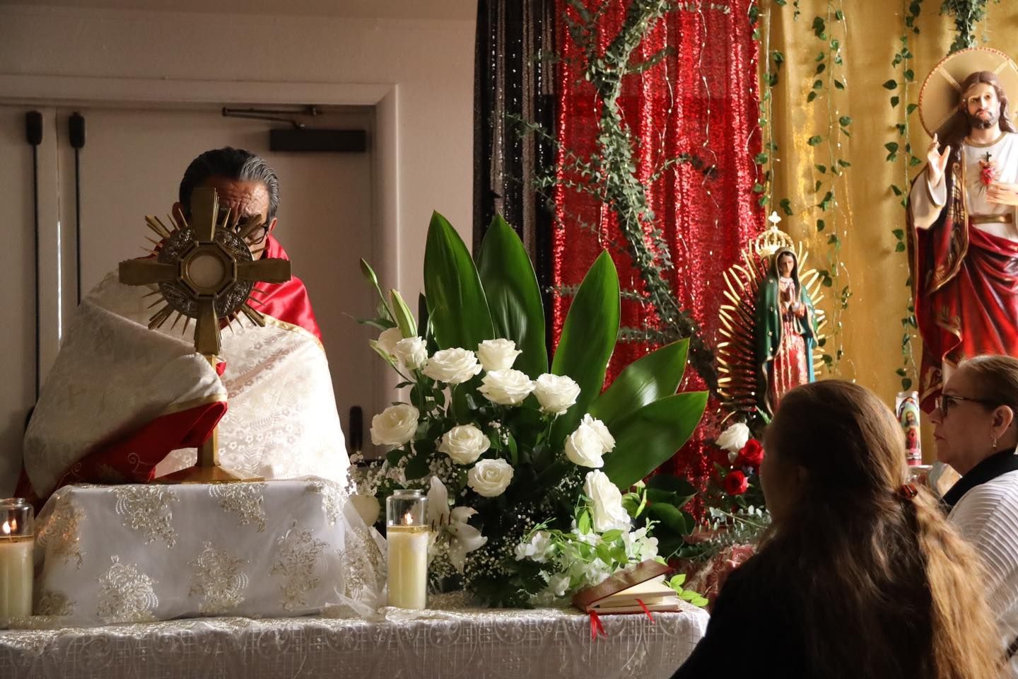 Religious altar with a decorated monstrance, white flowers, candles, and statues in a church setting