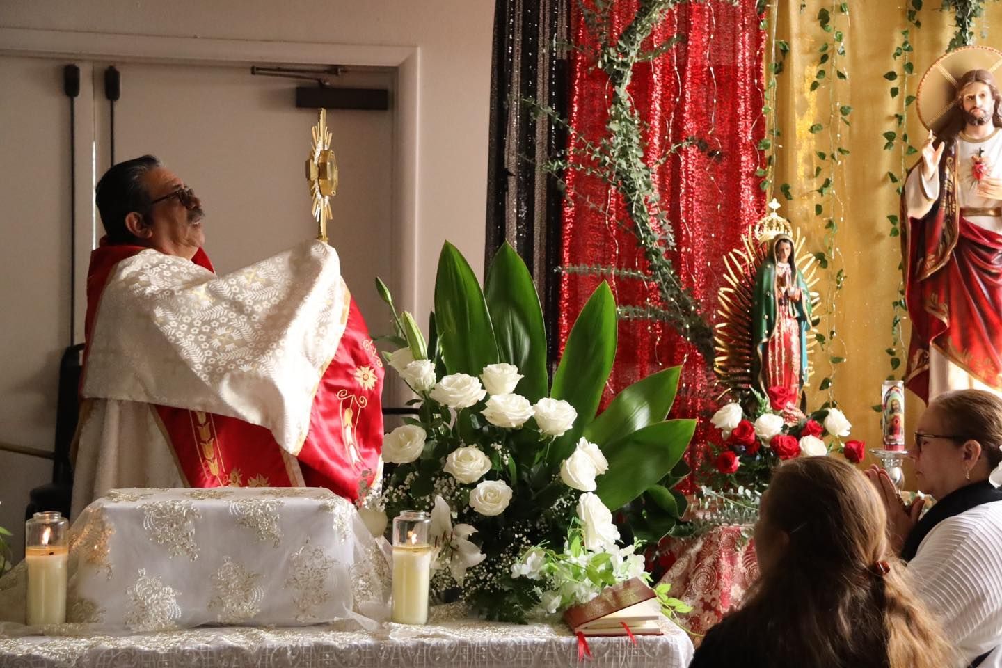 Priest holding a chalice at an altar during a church ceremony, with candles, flowers, and attendees nearby
