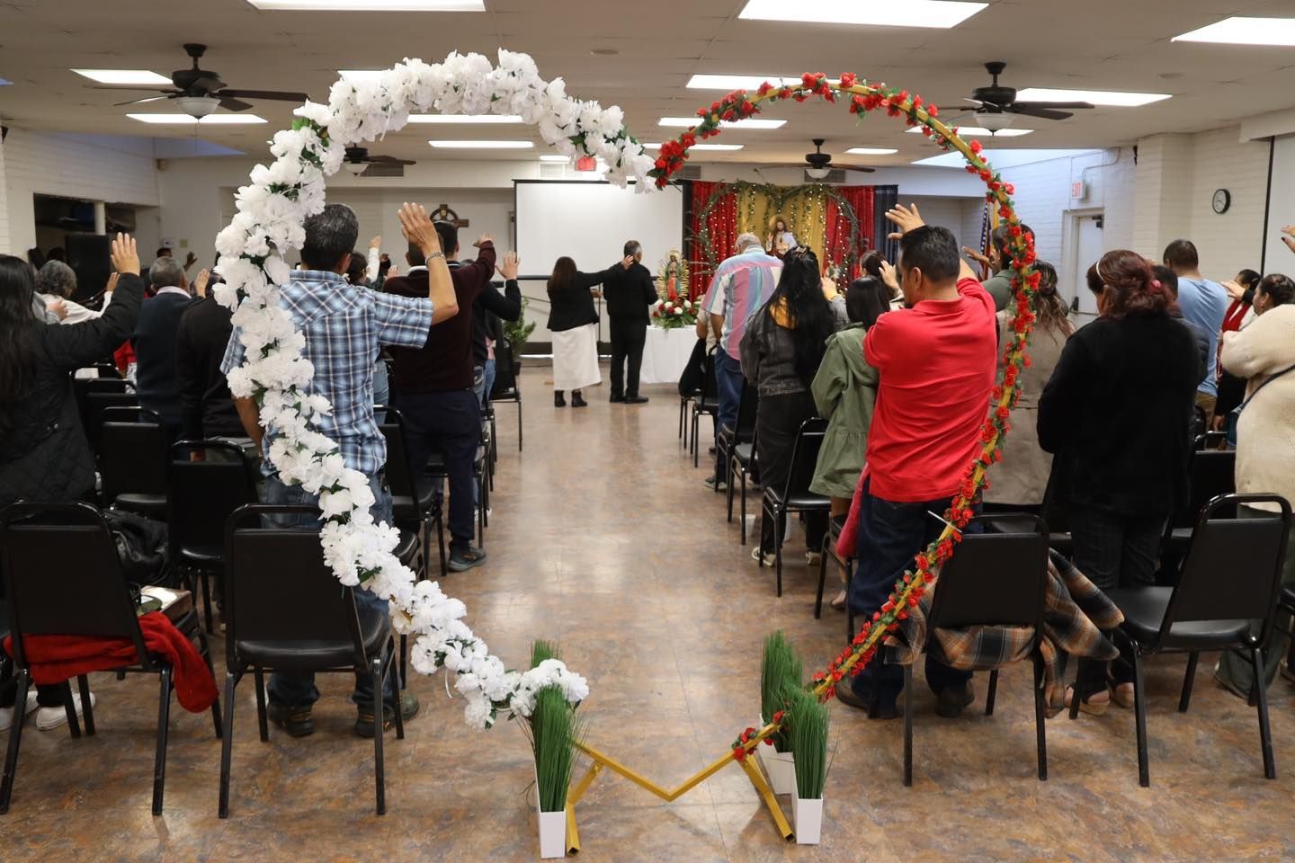 People gathered in a hall, viewing a heart-shaped arch made of white and red flowers.