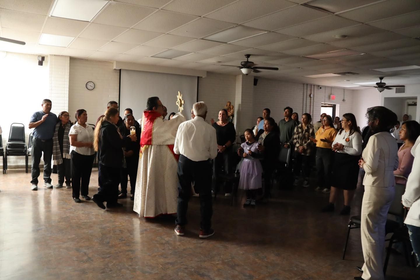 People gathered in a hall for a social event, with a white-robed person near the center.