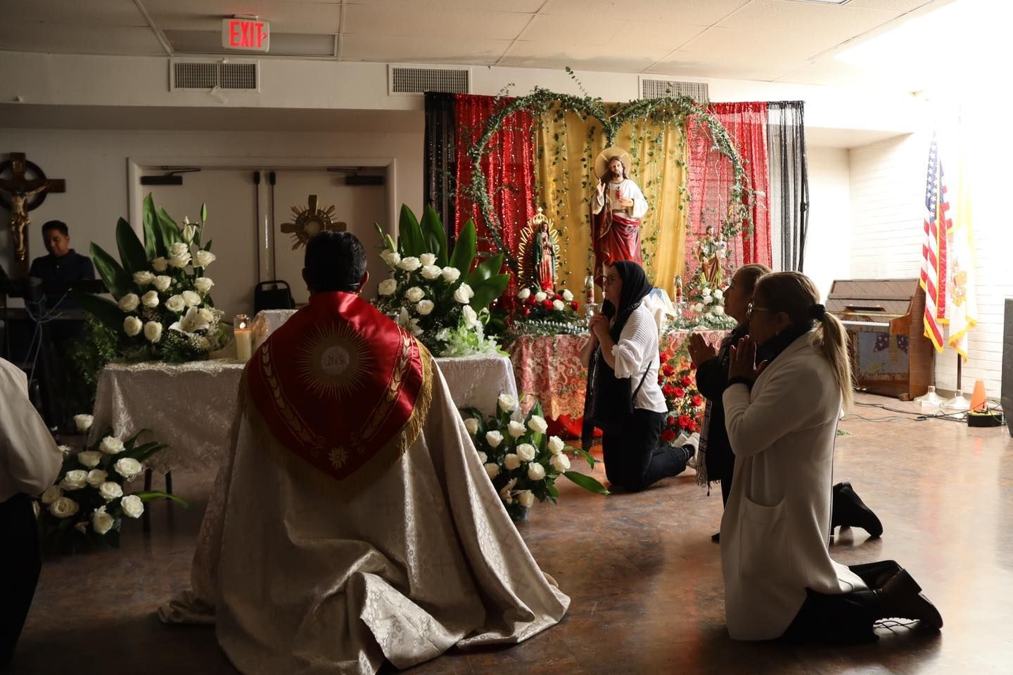 Two kneeling people in a church altar ceremony with flowers and a decorated backdrop.