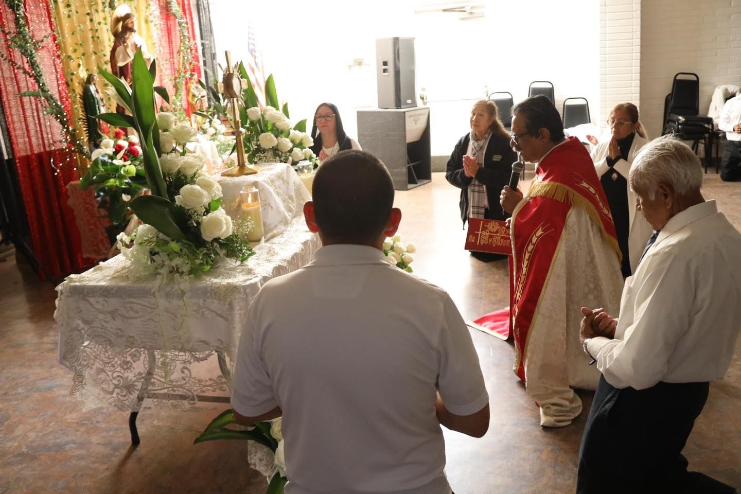 People gathered around a floral altar during a ceremony in a bright indoor room