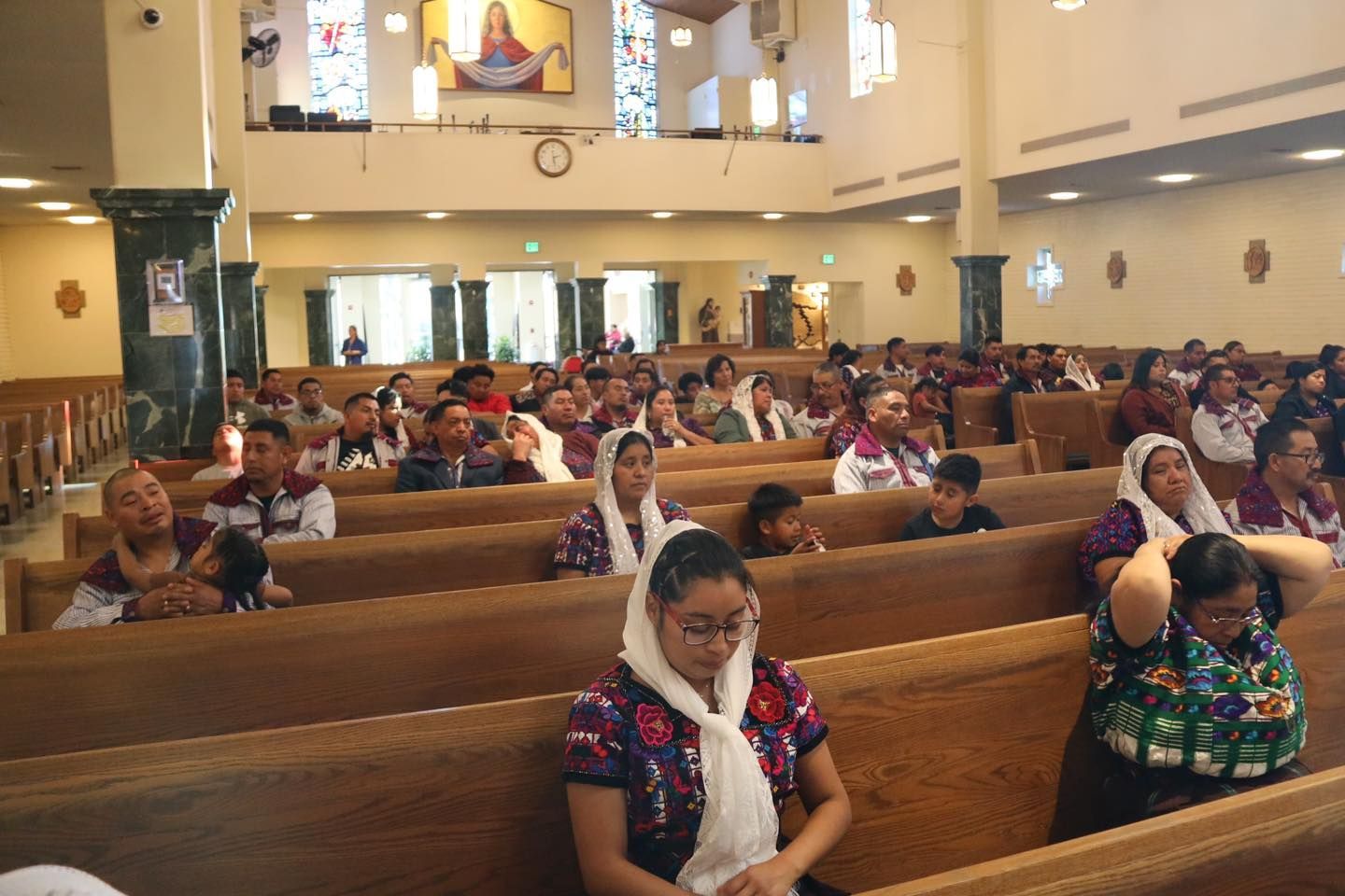 People seated in wooden pews inside a church, facing forward during a service.
