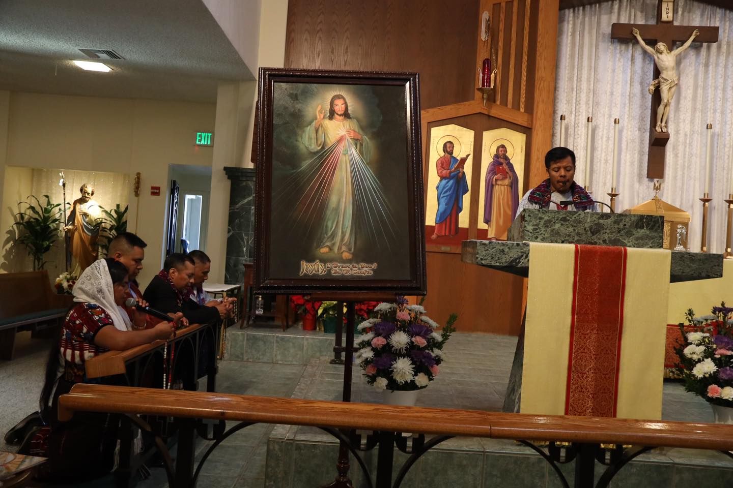 Church altar with priest at the lectern, crucifix and religious paintings, worshippers seated nearby