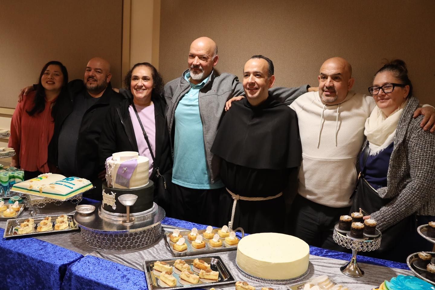 Group of people smiling behind a dessert table with cakes and pastries at a celebration