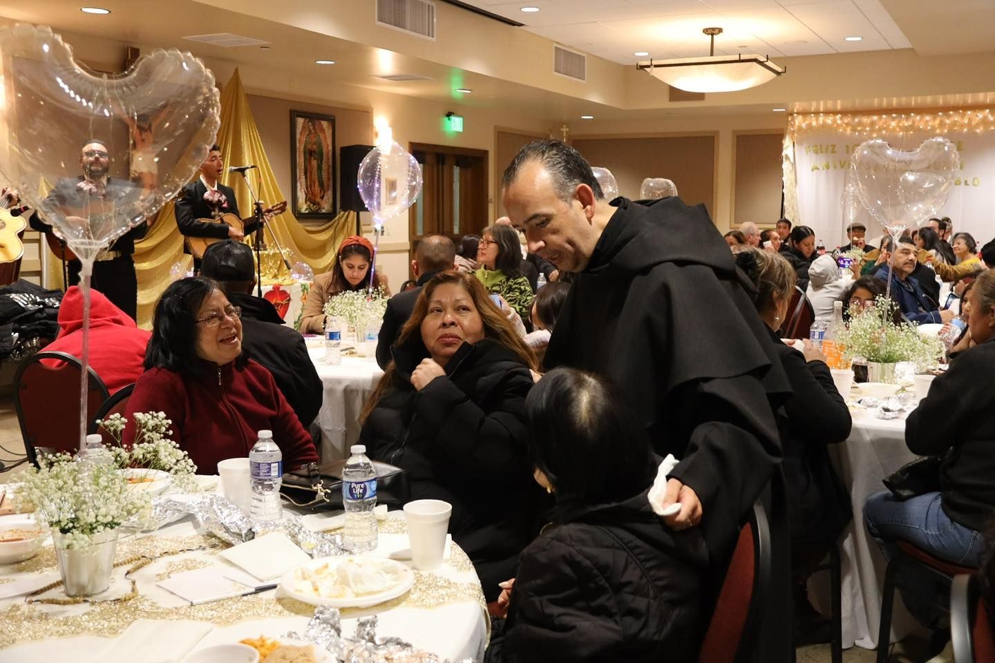 People seated at a warmly lit banquet table, talking and eating at a festive indoor gathering.