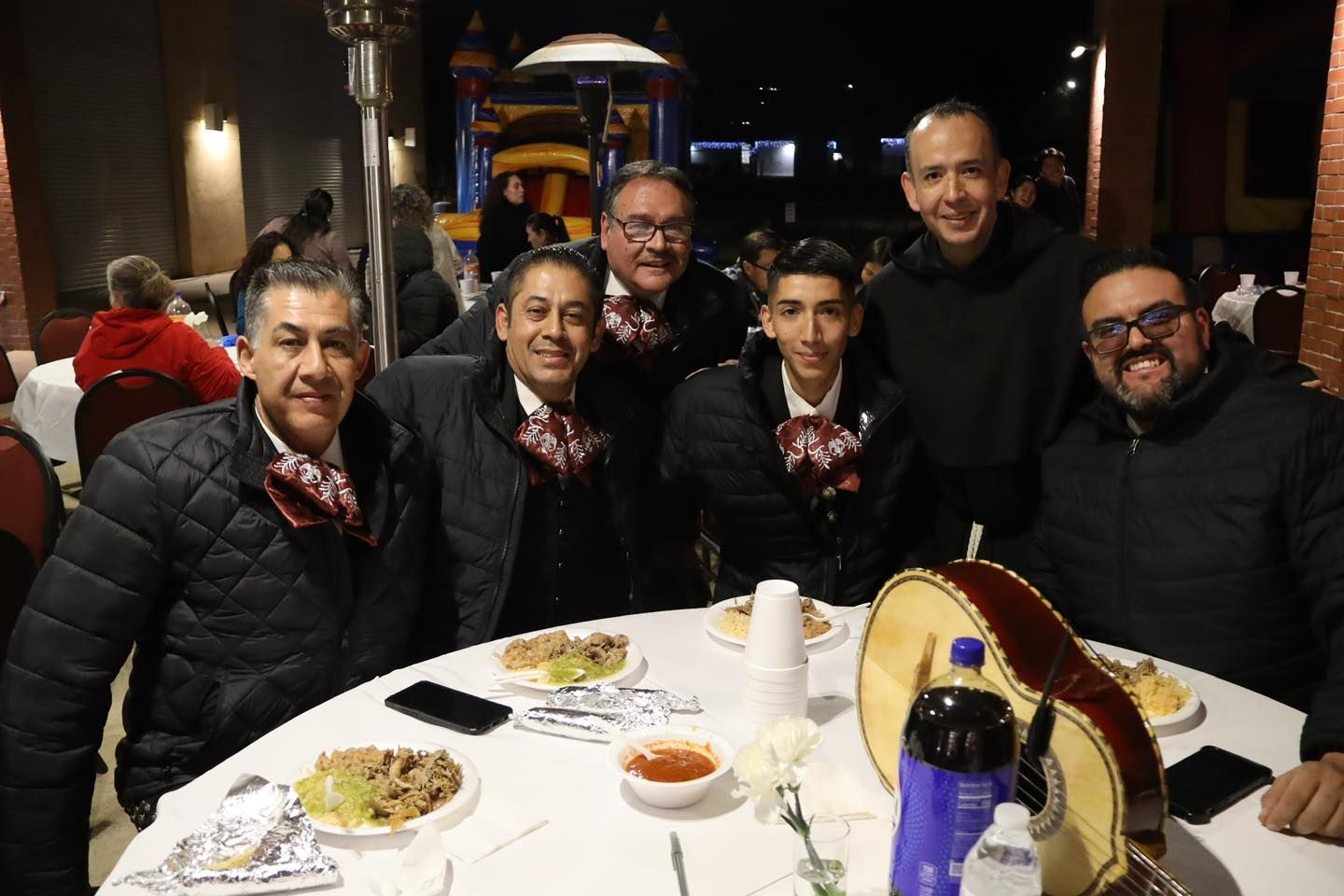 Six people seated at a restaurant table, smiling for a group photo with food and drinks.
