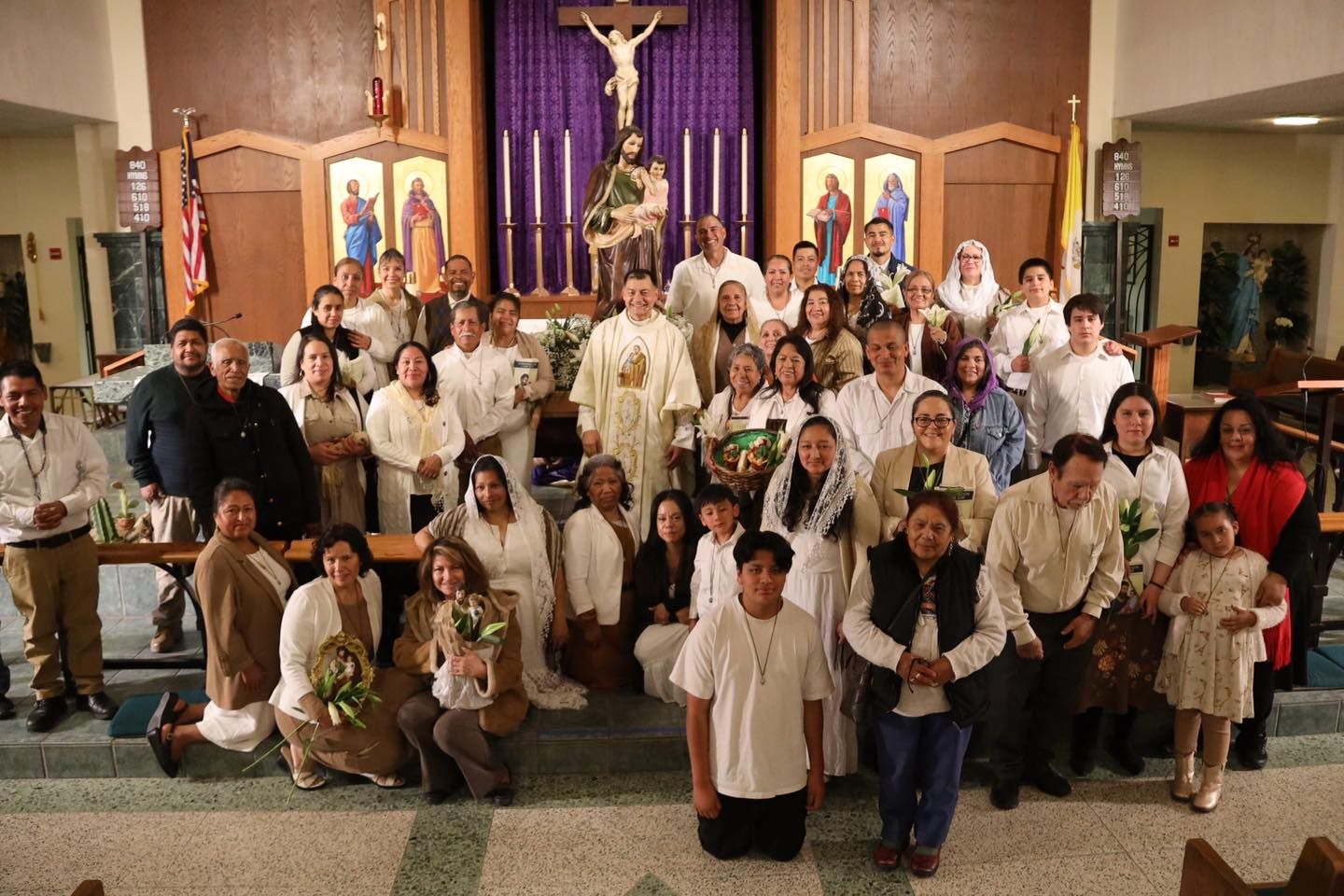 Large group posing in a church sanctuary in front of a crucifix and purple altar cloths