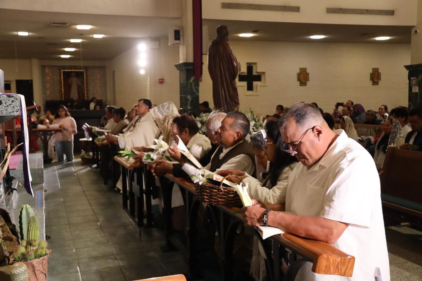 People standing in a church aisle, reading books during a service.