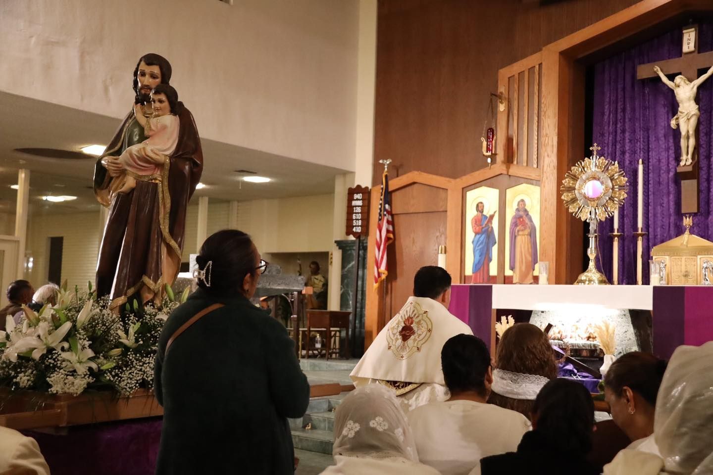 Church altar with a saint statue, candles, and worshippers kneeling in prayer