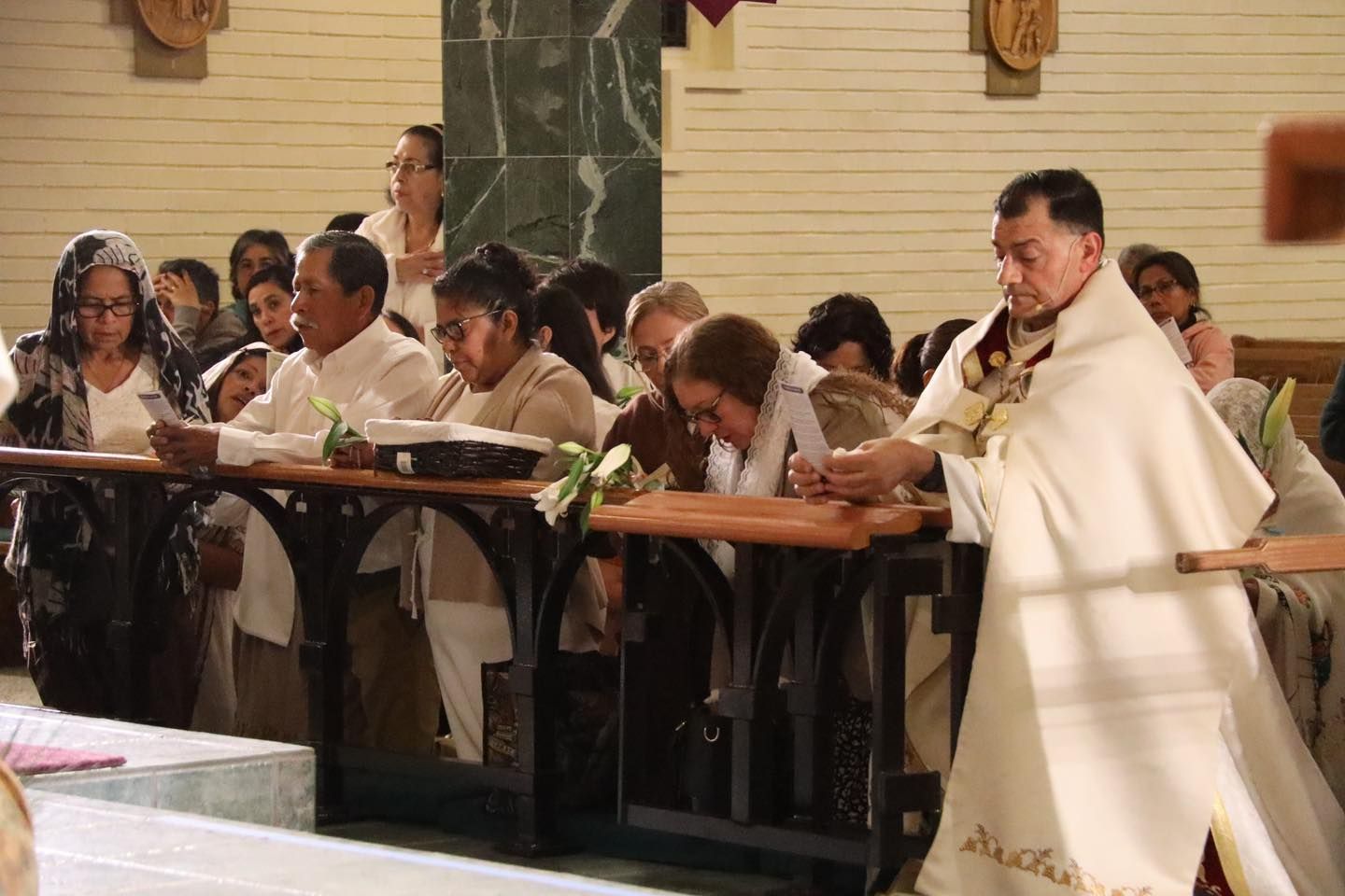 People praying in a church, with a priest in white robes at the front by the altar