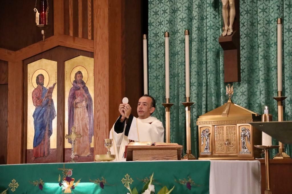 Priest elevating the Eucharist at an altar in a church, with icons and candles behind him