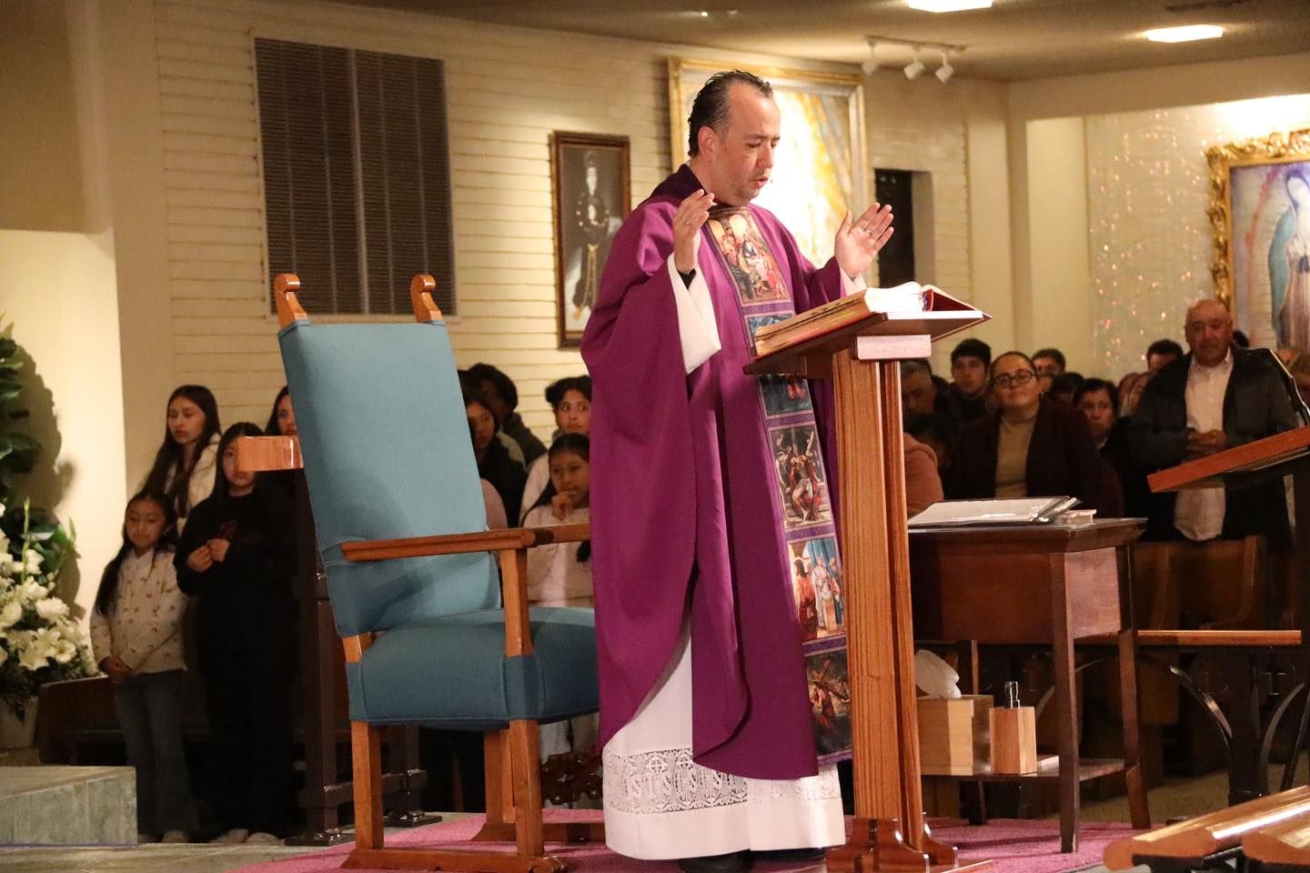 Priest in purple vestments speaking at a church lectern before a congregation