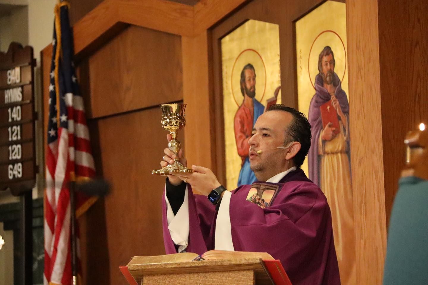 Priest in purple vestments holding up a chalice at a church altar with religious icons behind him