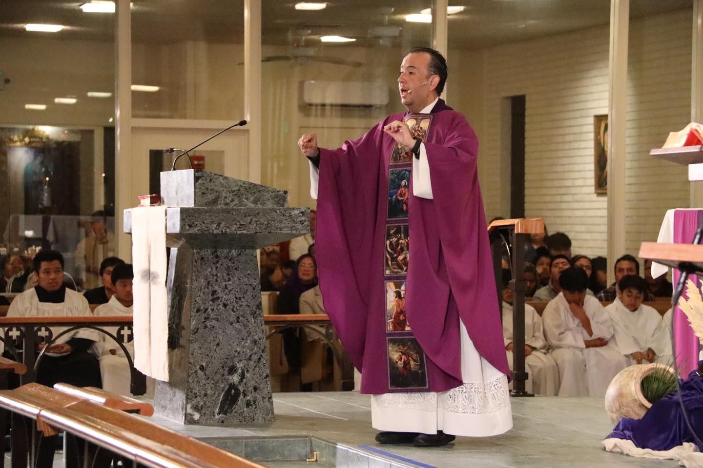 Priest in purple vestments speaking at a church altar during Mass