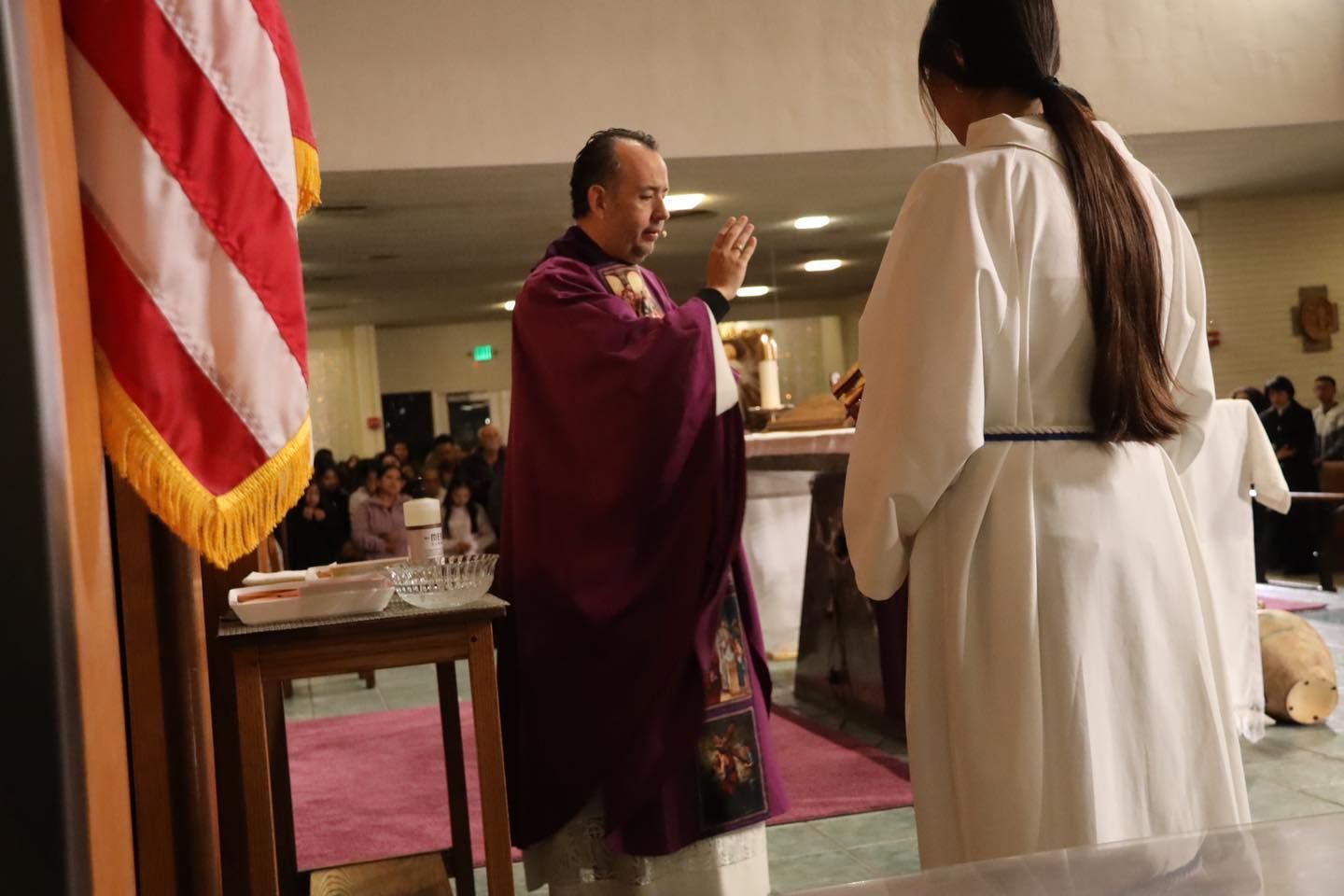 Priest in purple robe blesses a person in a white robe during a church ceremony