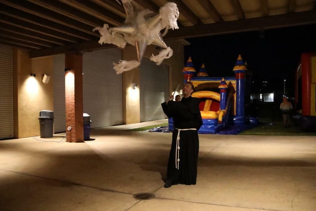 Person in black robe beneath a white hanging sculpture at night, with an inflatable bounce house in the background