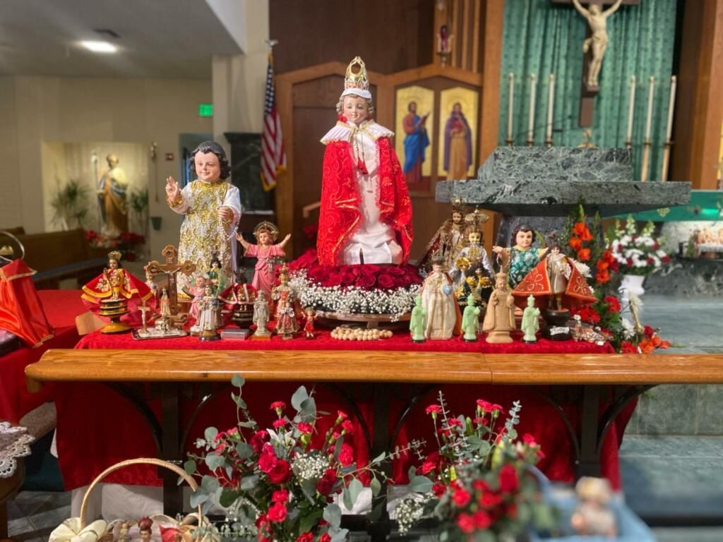 Ornate altar with many small statues and red flowers beneath a central crucifix in a church sanctuary