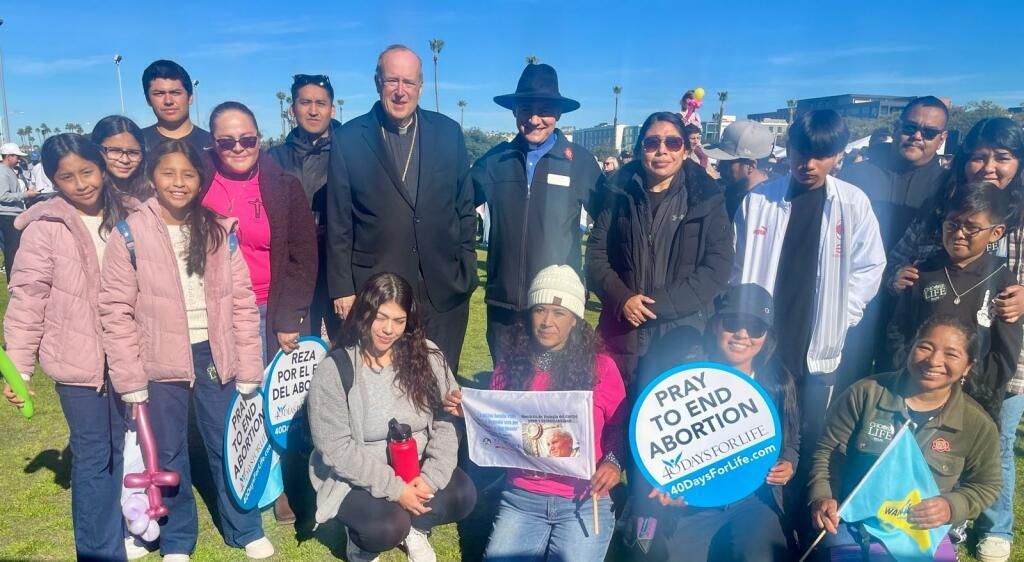 Group posing outdoors holding signs at a community event on a sunny day