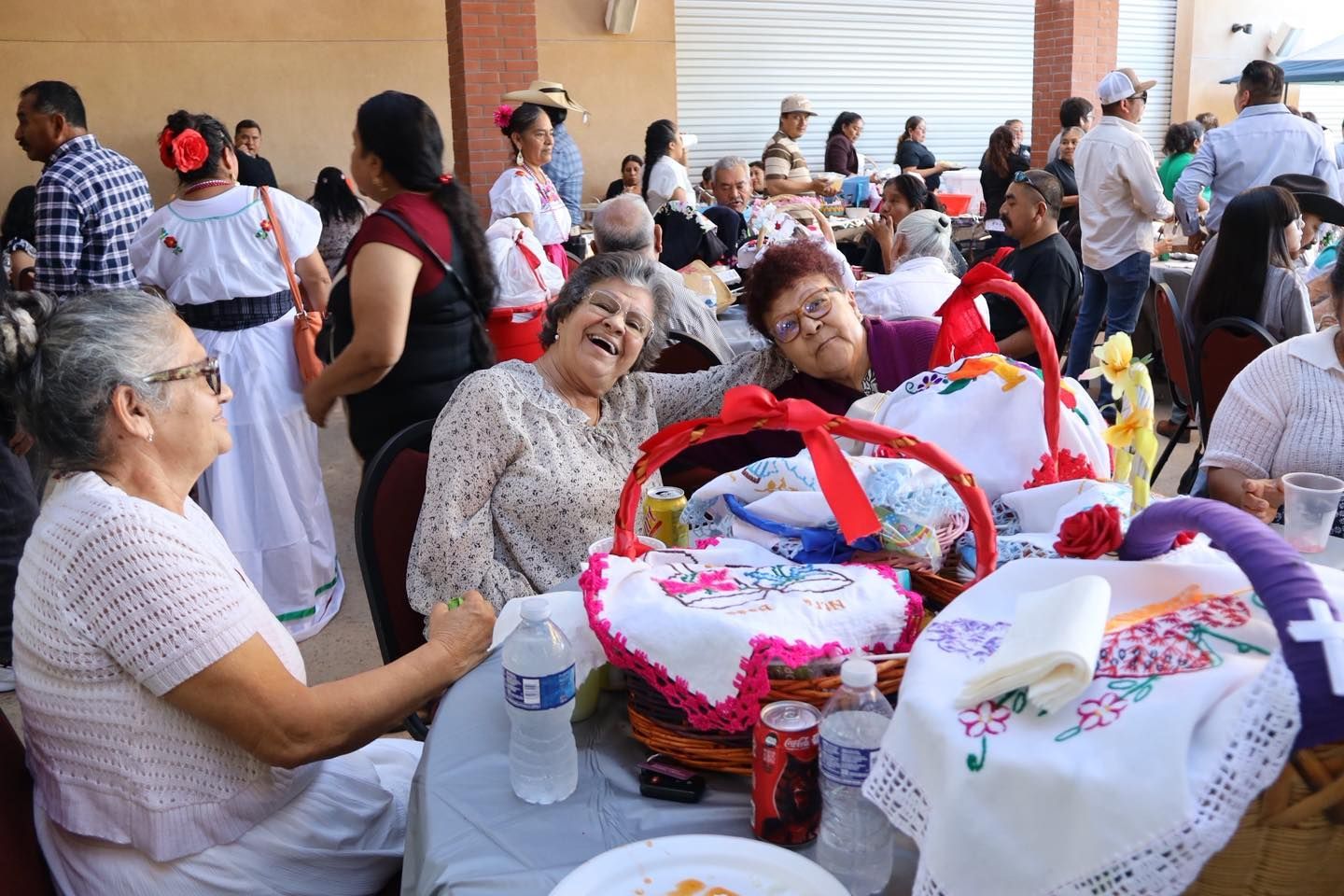 People seated at a picnic table with gift baskets and colorful decorations in an outdoor gathering