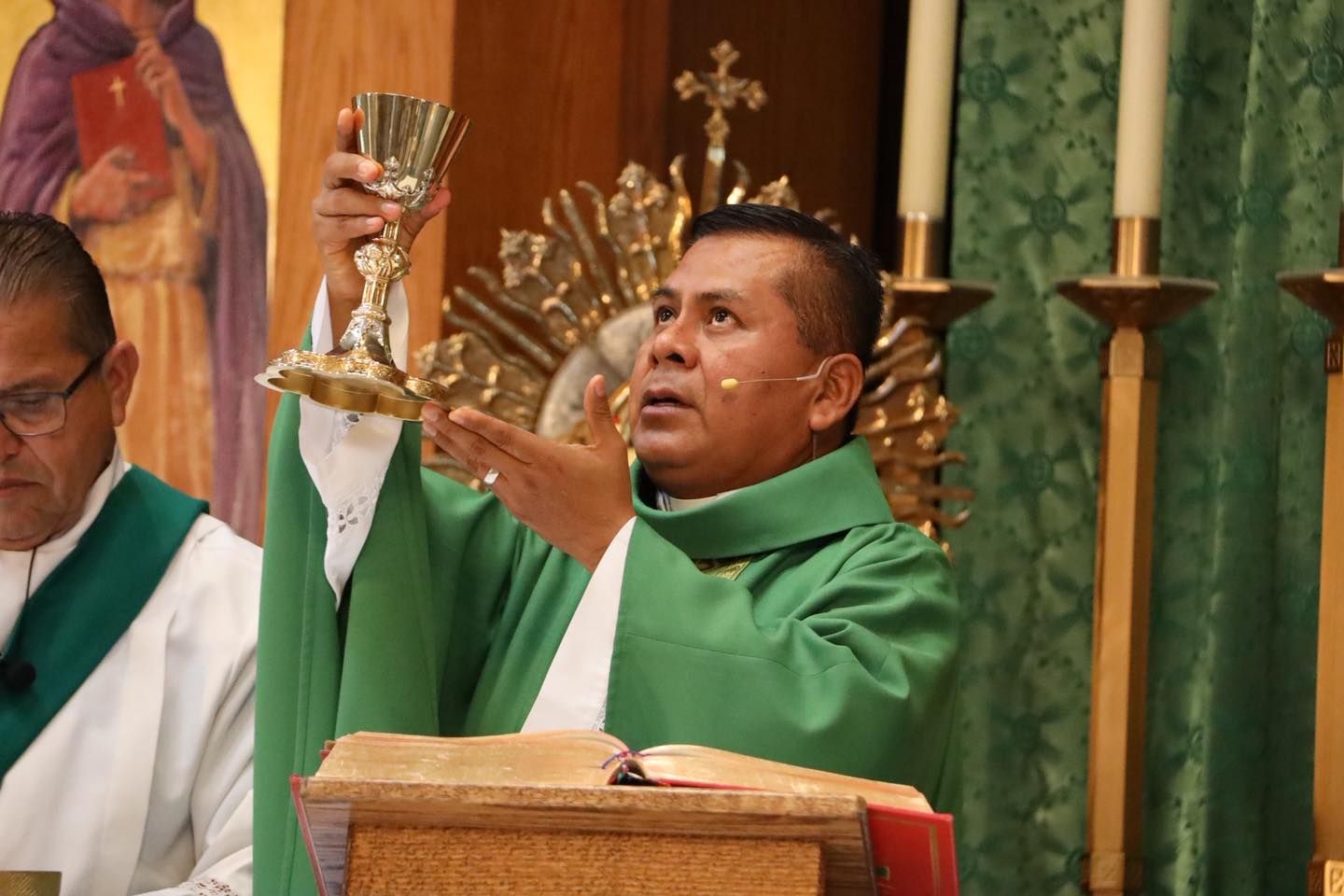 Priest in green vestments lifting a chalice during Mass at the altar