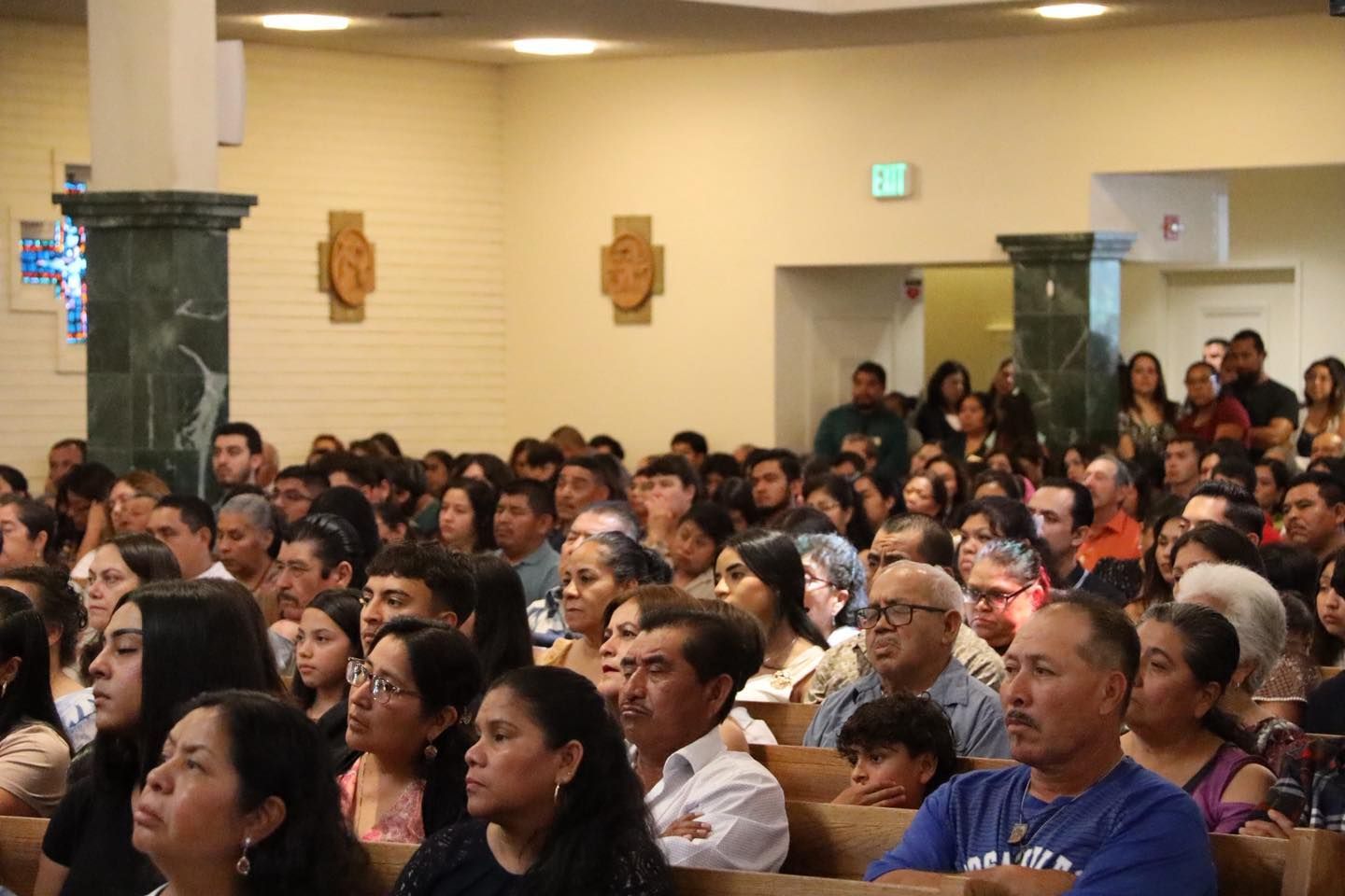 Crowded hall audience seated and standing, listening attentively during an indoor event
