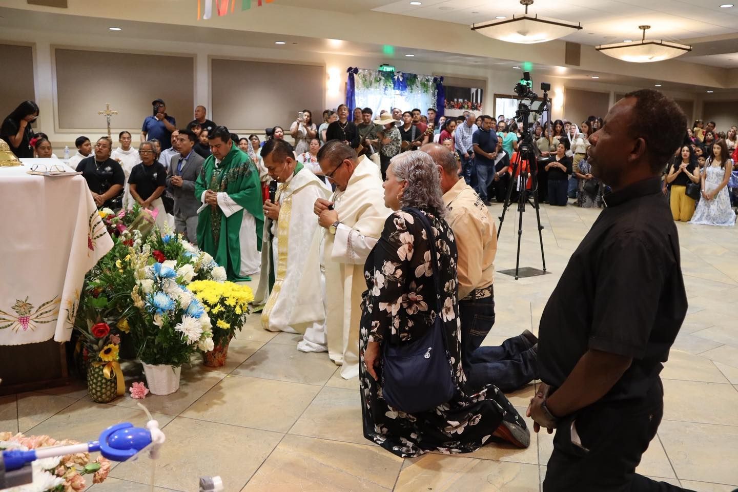 People kneeling in a church beside a flower-covered altar during a ceremony