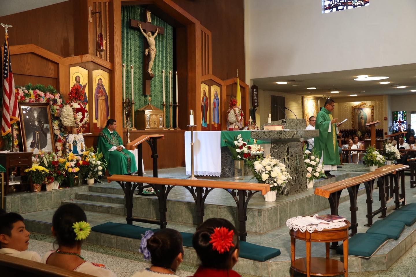 Church altar with green-robed clergy, flowers, and an audience seated in pews