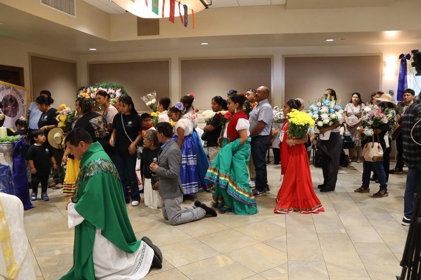 Masked dancers in colorful costumes performing in a crowded indoor hall during a festive event