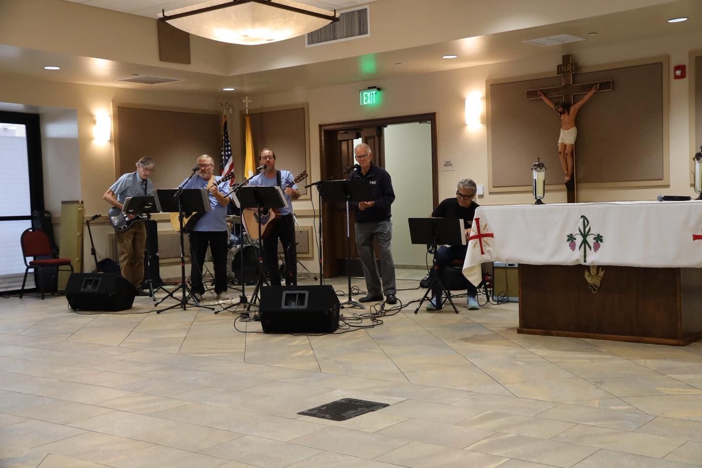 Musicians performing in a church sanctuary beside the altar, with instruments and microphones arranged onstage.