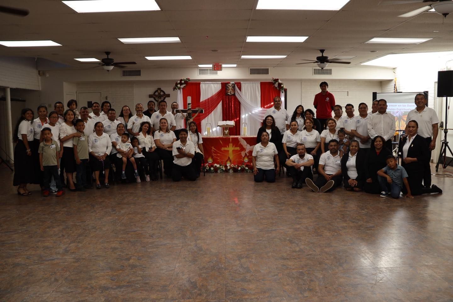 Large group posing in a hall, wearing white shirts in front of red and white decorations