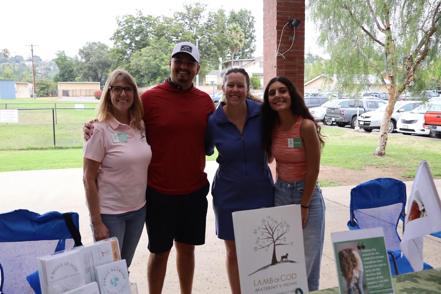 Four people stand behind a table at an outdoor booth with display boards and flyers.