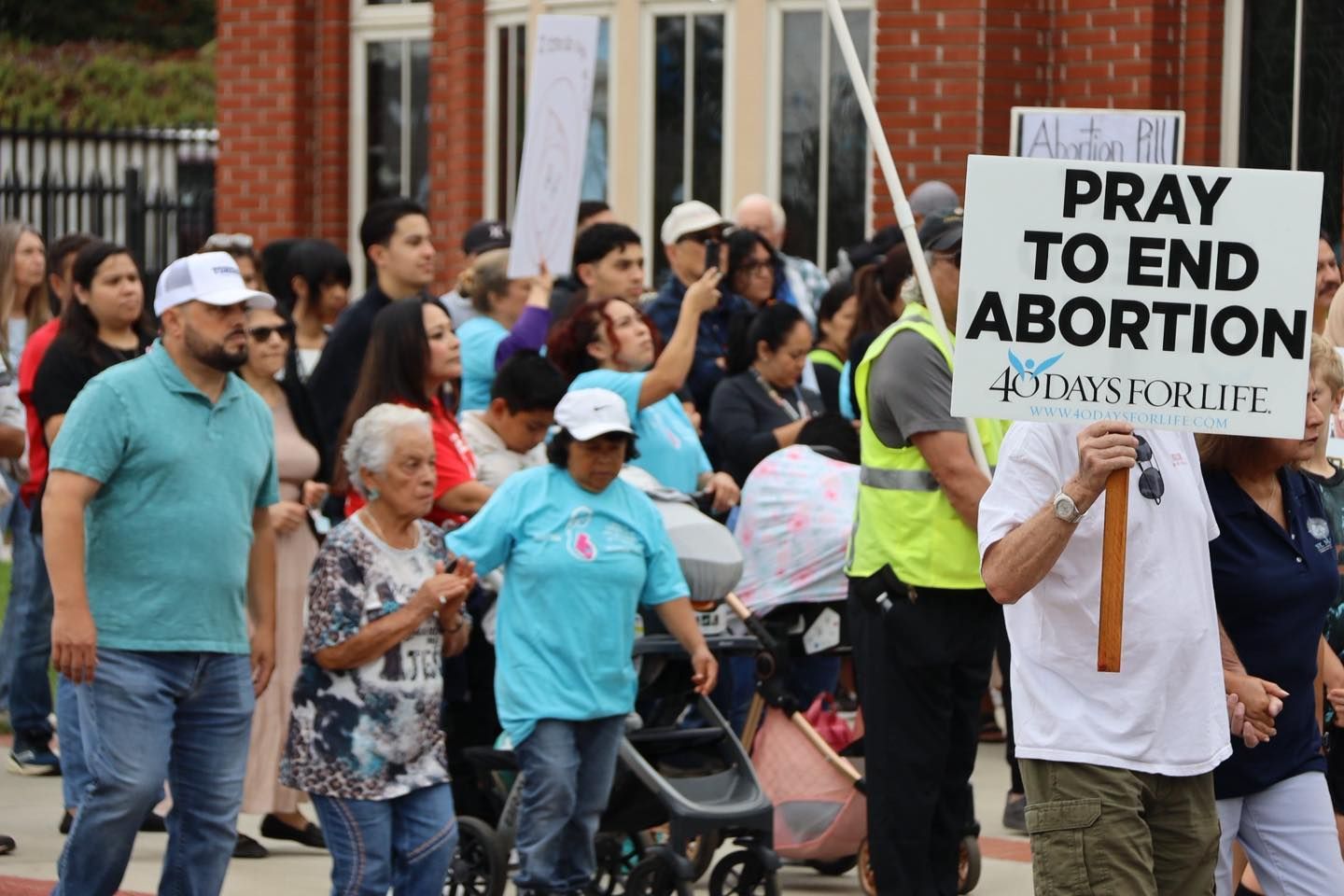 Crowd of protesters holding signs, including one that reads “Pray to end abortion,” at a public march.