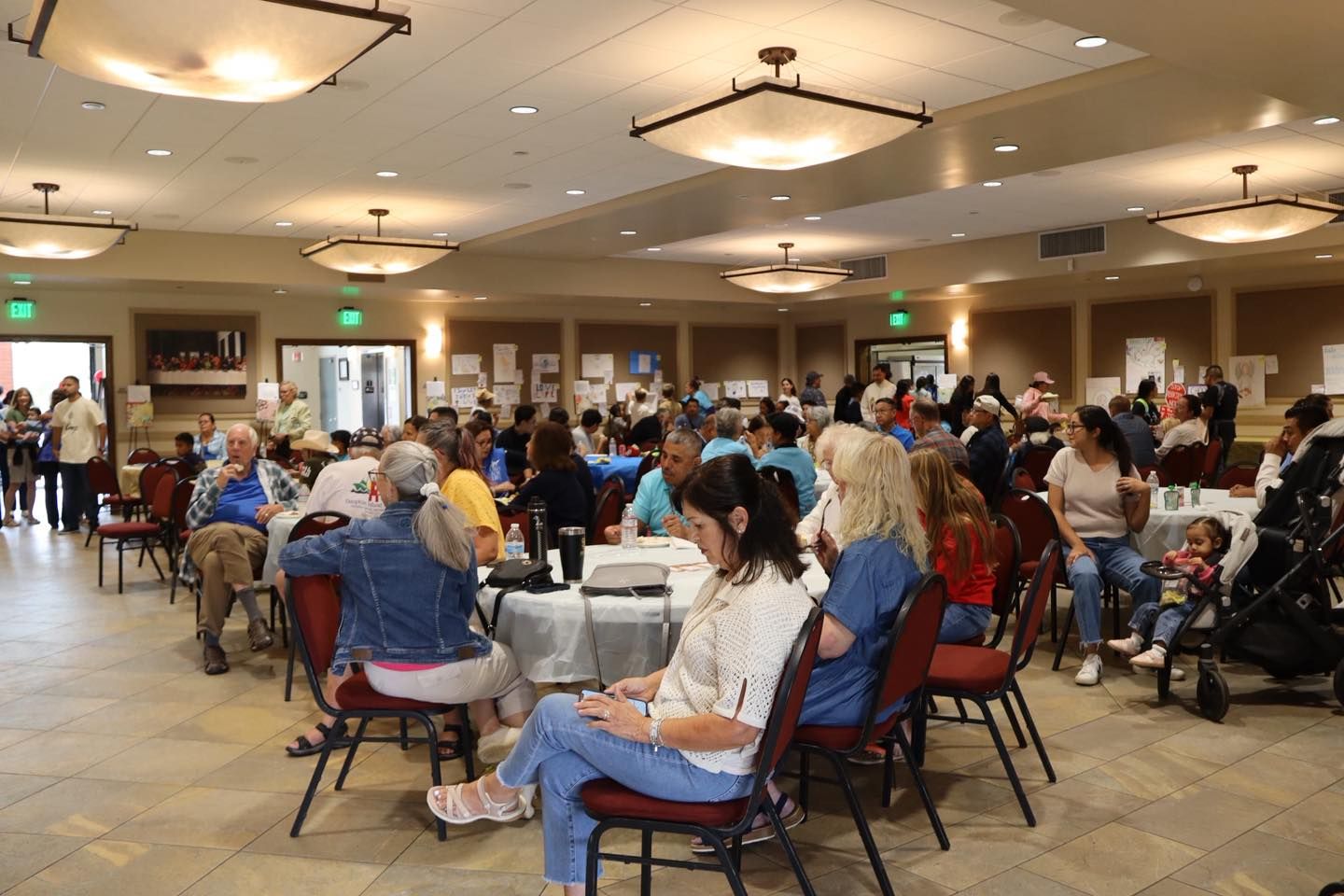 People seated at round tables in a bright banquet hall, gathered for a social event.