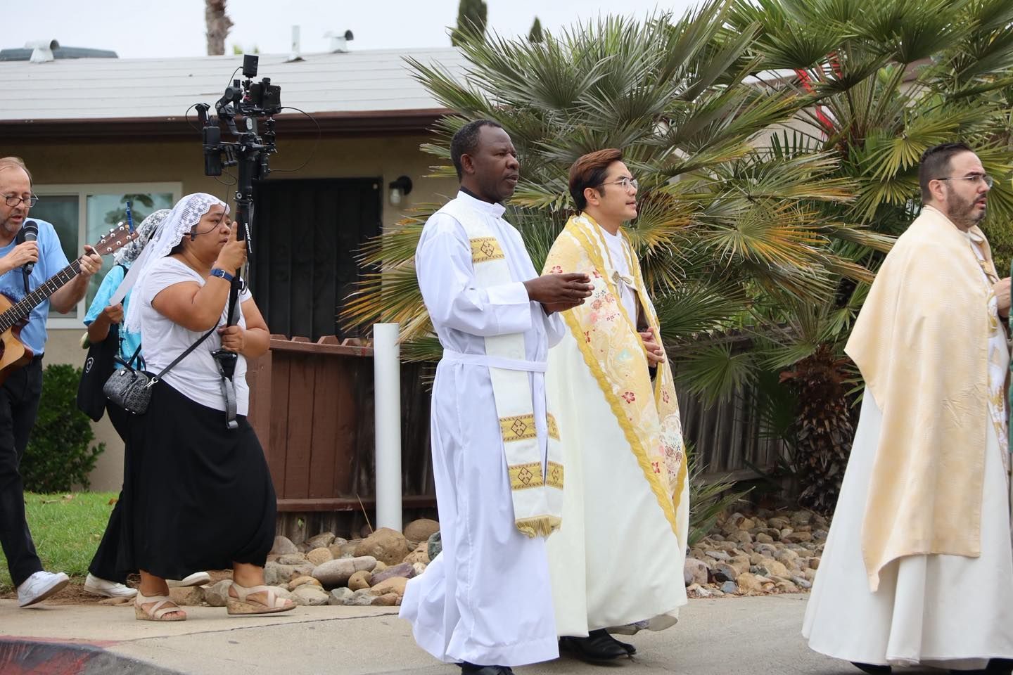 People in white and gold robes walking outdoors in a procession