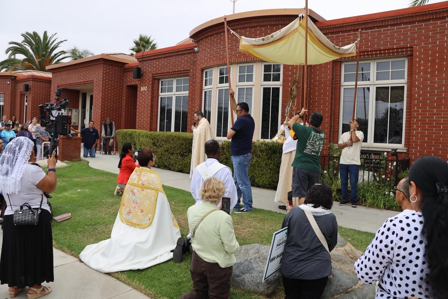 People kneeling and standing at an outdoor wedding ceremony beside a brick building