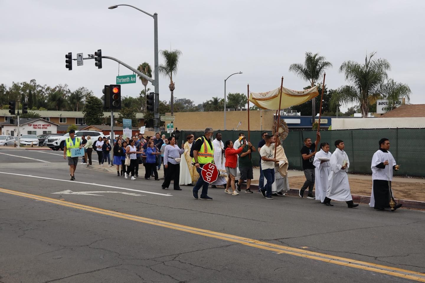 People walking in a street march at a city intersection, carrying signs and wearing white and dark clothing.