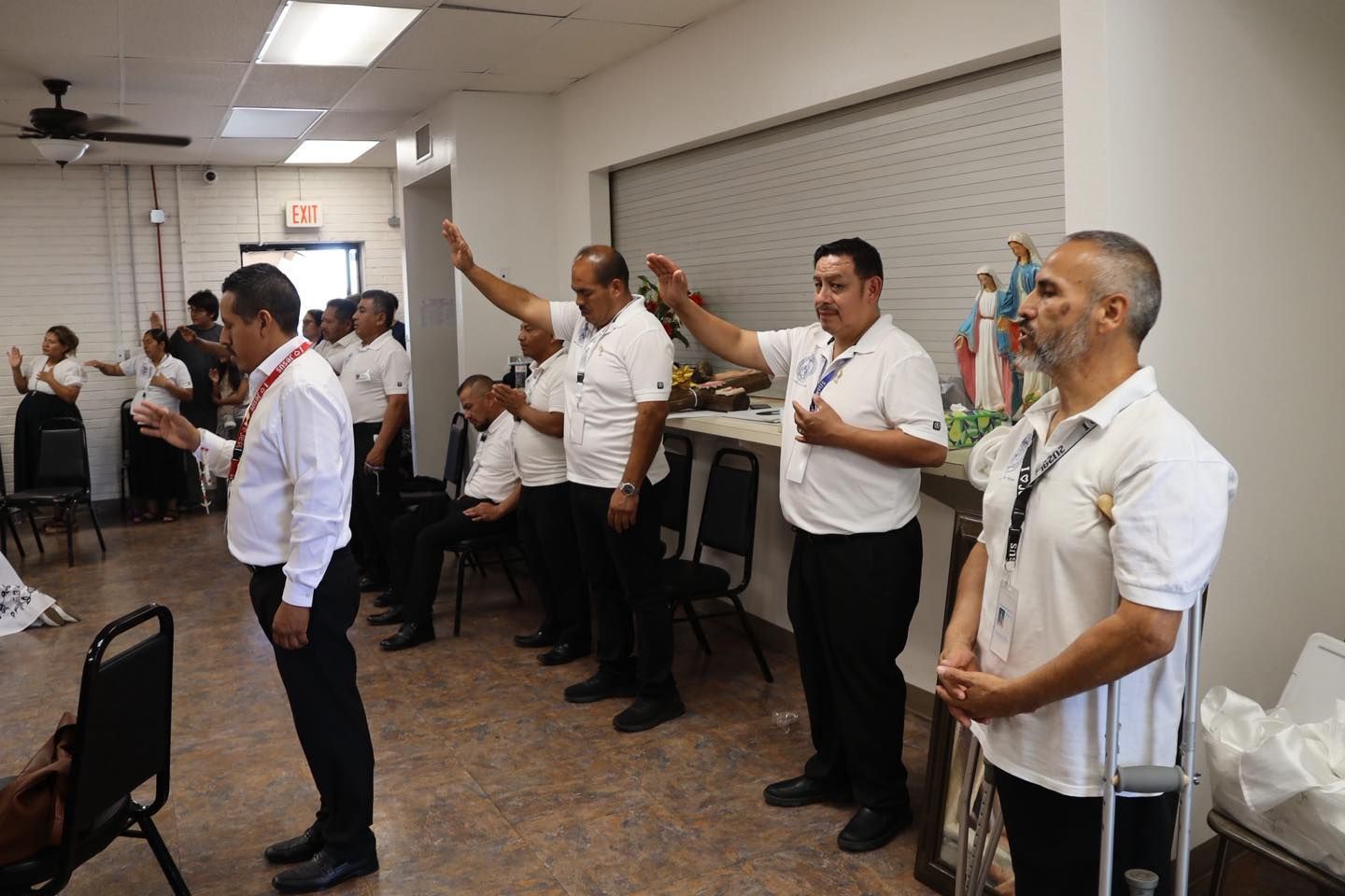 People standing in a room with one person raising a hand during a meeting or briefing
