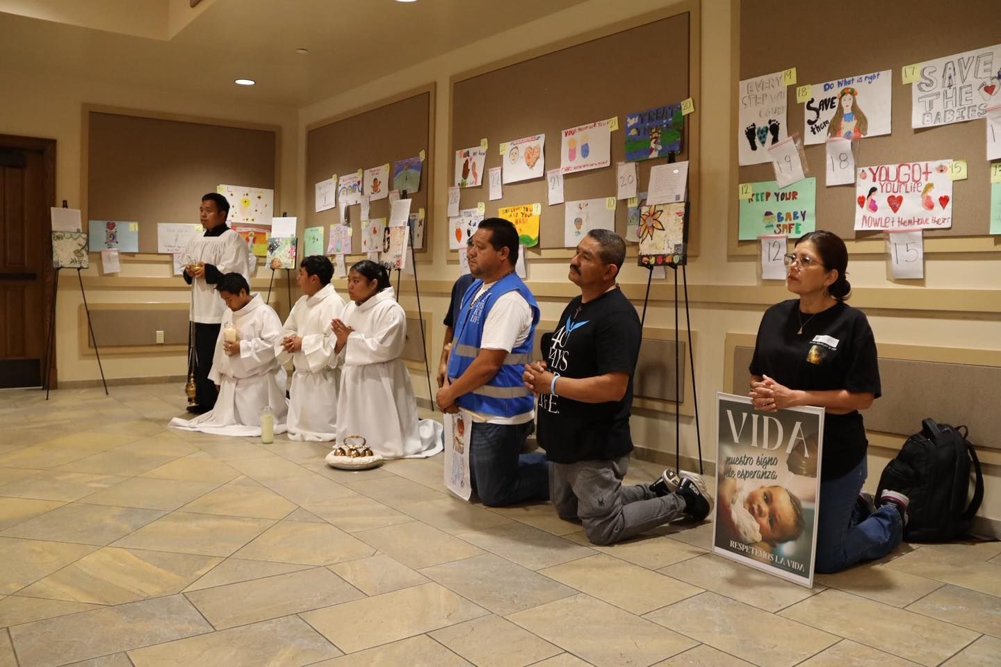 People kneel in a hallway beside posters and signs, holding memorial placards.