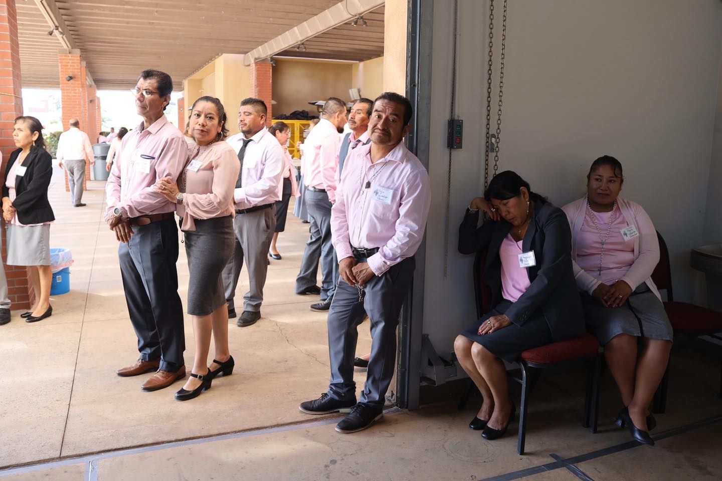 People standing and sitting in a hallway, waiting in line near a building entrance.