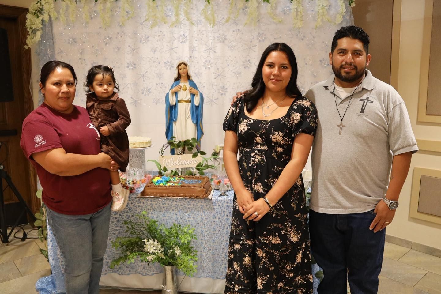 Four people pose beside a religious altar with a statue of the Virgin Mary and flowers.