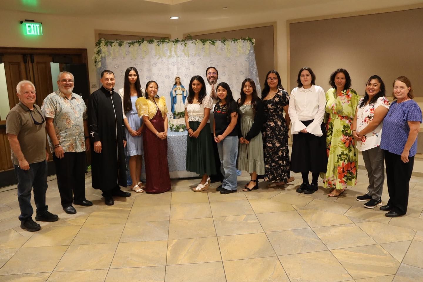 Group of people standing in a banquet hall, posing in formal and semi-formal attire.