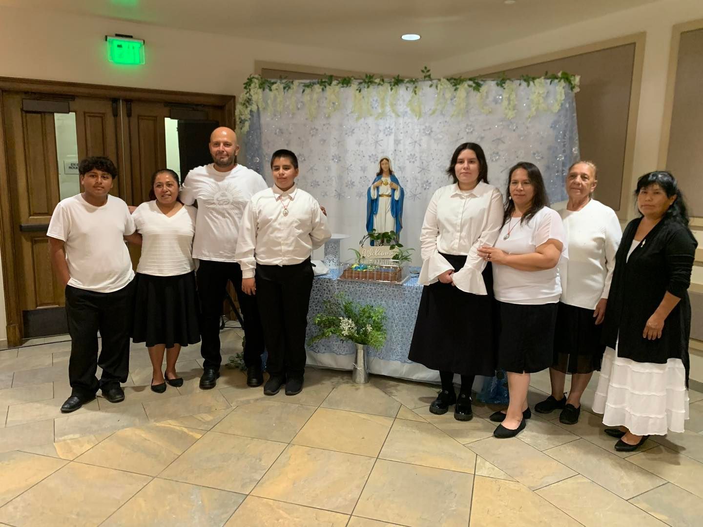 Group standing in a hall beside a small shrine with a statue and flowers.