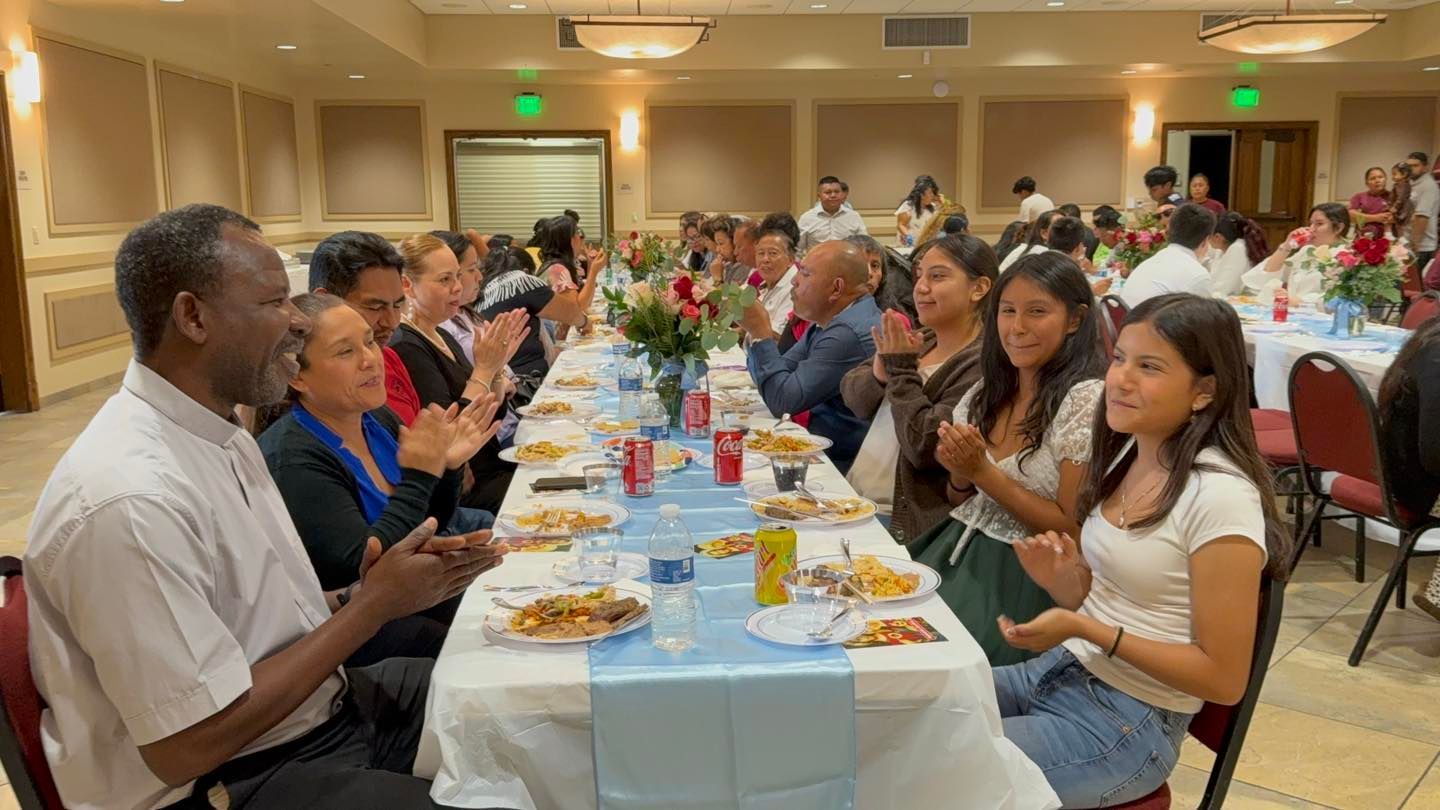 Banquet guests seated at a long table, clapping during a shared meal in a bright event hall