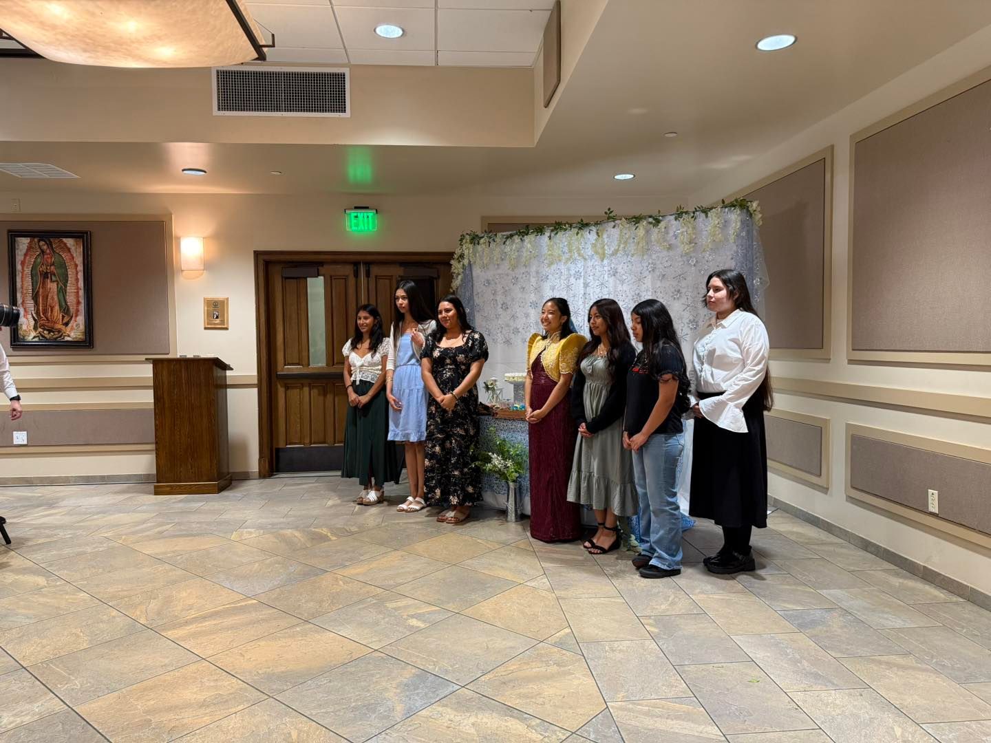 People standing in a line at a formal indoor event, posing near a white backdrop.