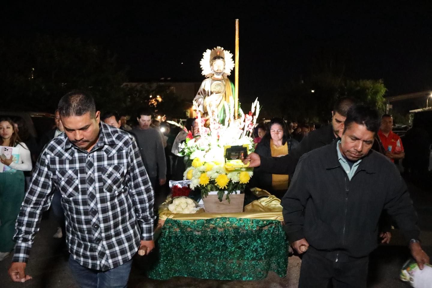 People carrying a decorated floral altar with candles at a nighttime outdoor procession