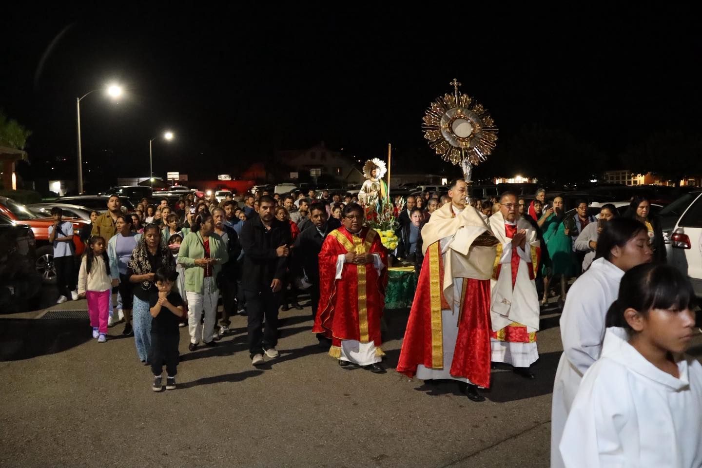 Night parade procession with people in red robes walking through a parking lot at night