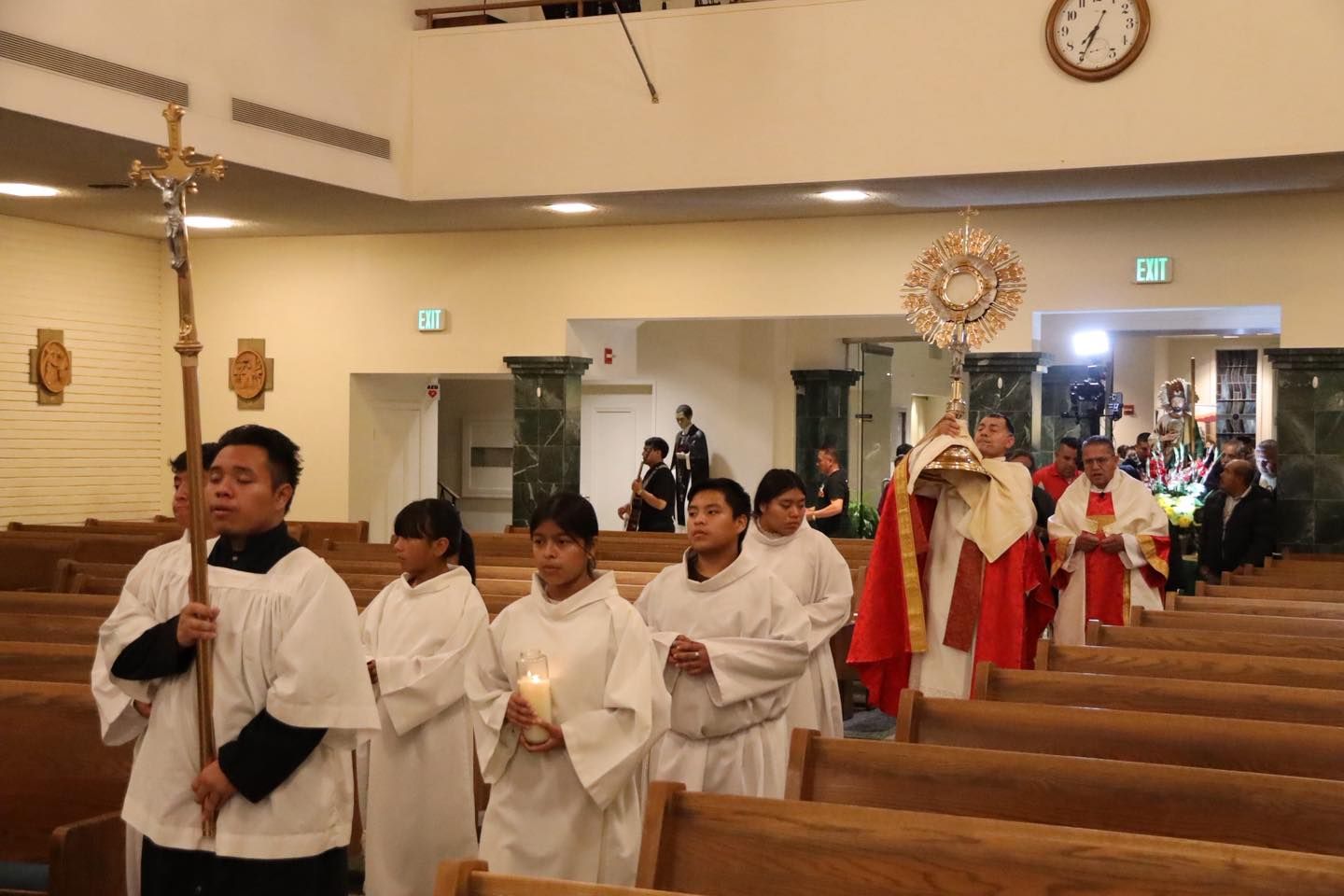 Church procession with altar servers in white robes carrying candles and a cross down the aisle